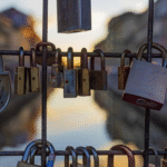 Locks hanging on a transparent metal fence with a stream and mountains in the distance, symbolizing unlocking leadership potential and moving forward toward goals at sunset.