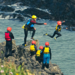 Instructor guiding a child into a river between cliffs, symbolizing trust, transparency, and shared risk in leadership.