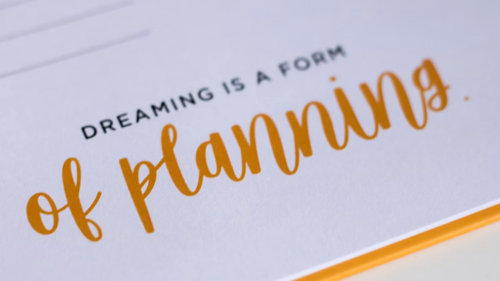 Open notebook with handwritten words reading "dreaming is a form of planning"