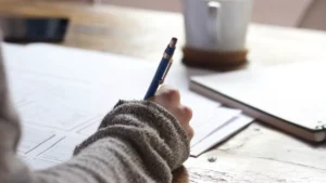 Woman's hand writing notes at a desk with a coffee cup in the background planning the year end campaign.